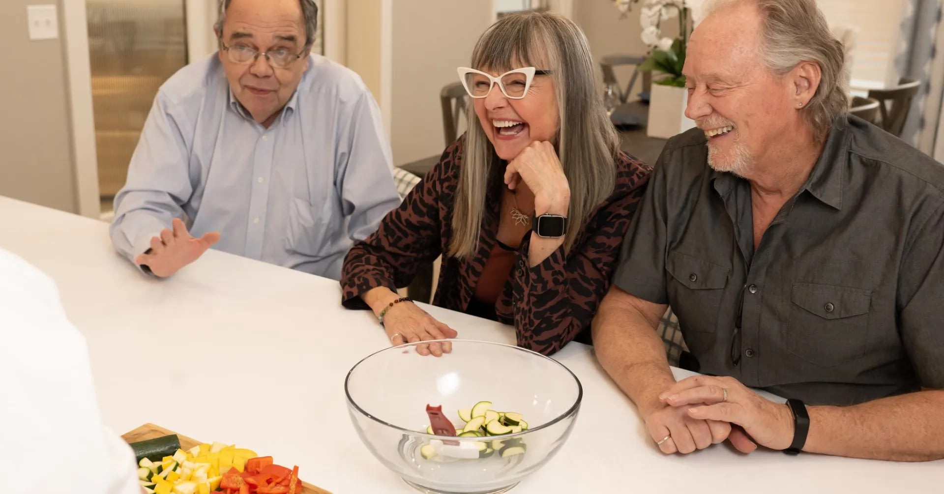 Three seniors laughing at table with fresh vegetables