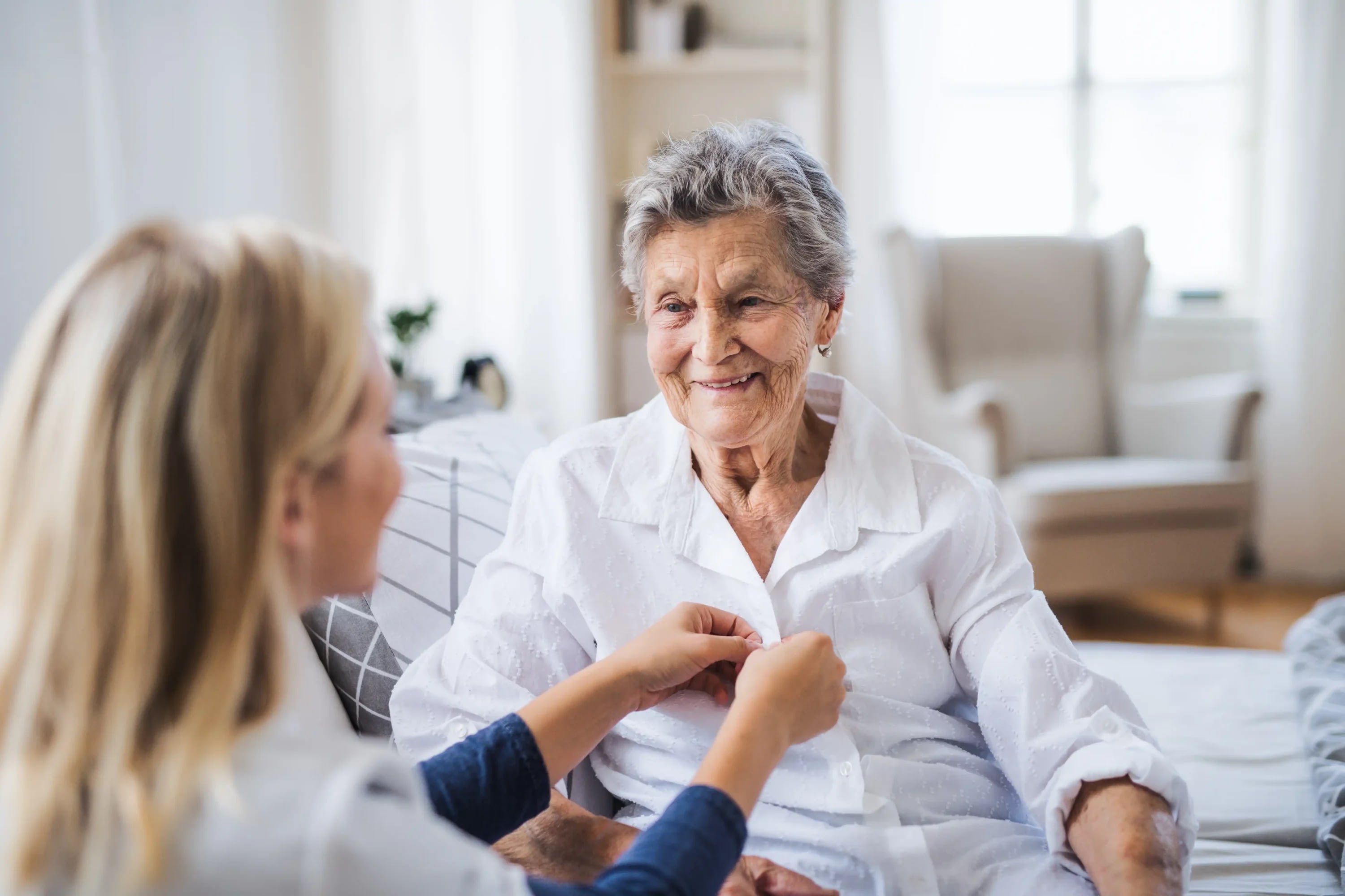 Caregiver helping elderly woman button shirt at home