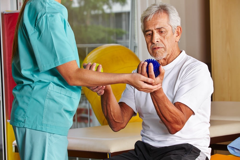 Senior man doing hand therapy with caregiver