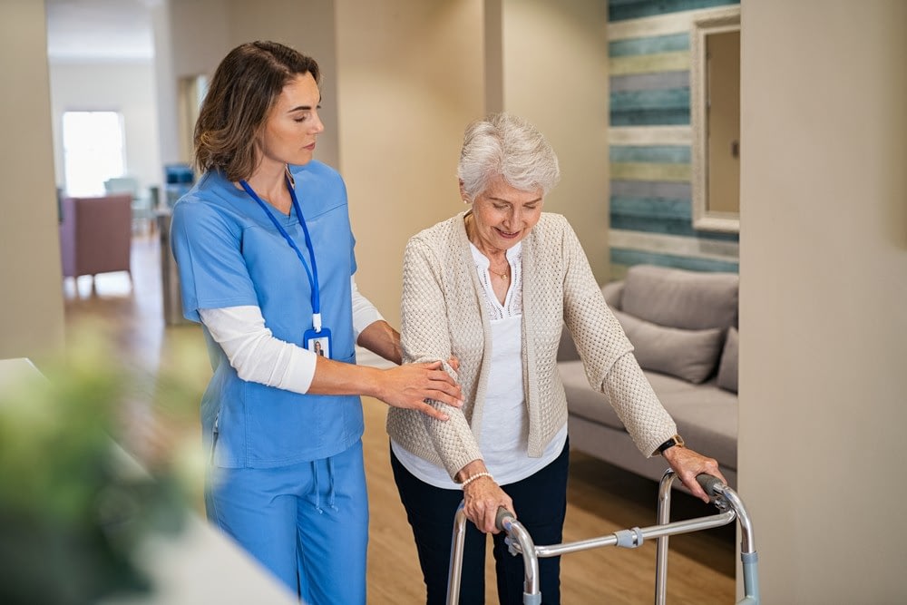 Caregiver assisting elderly woman with walker indoors