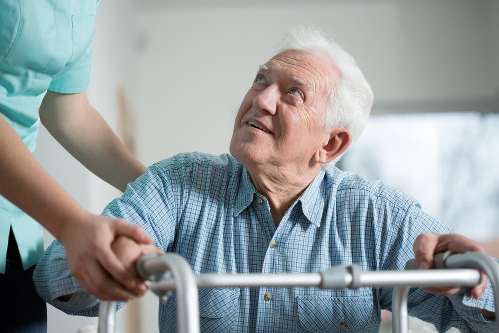 Elderly man using walker with caregiver support