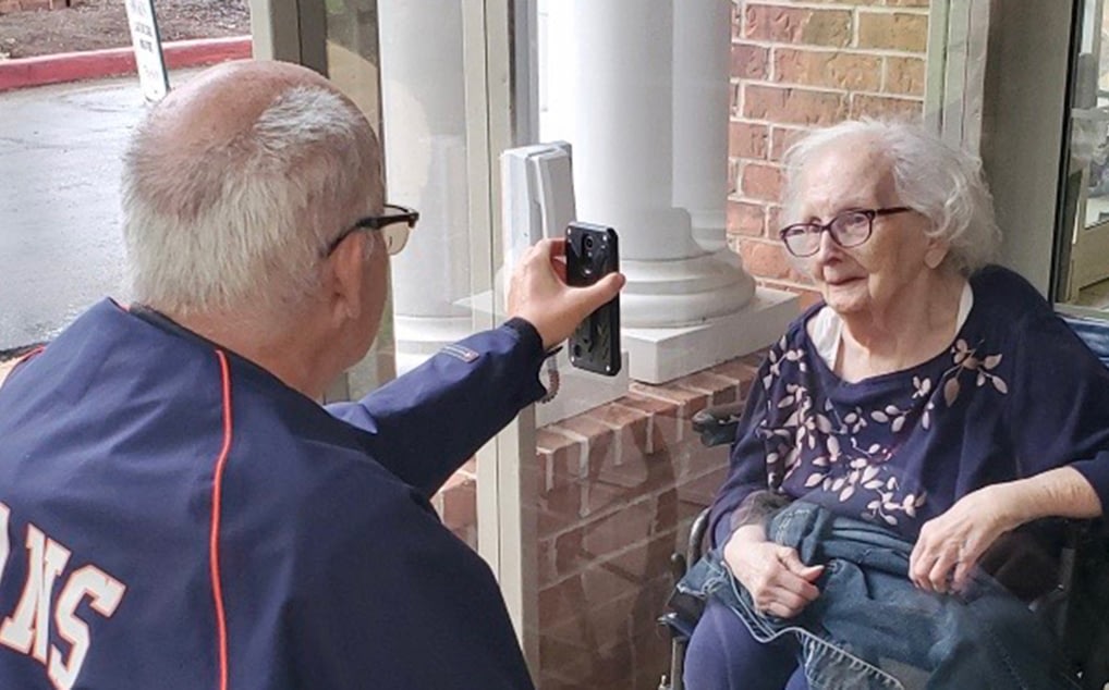 Man photographing elderly woman in wheelchair outside building
