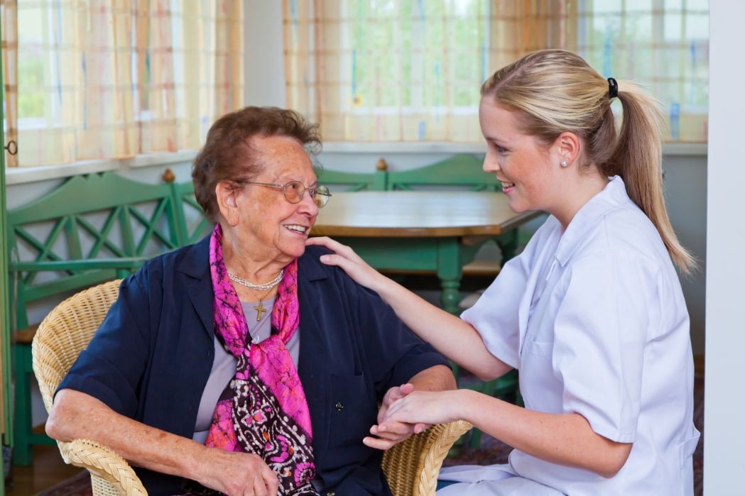Caregiver comforting elderly woman in bright room