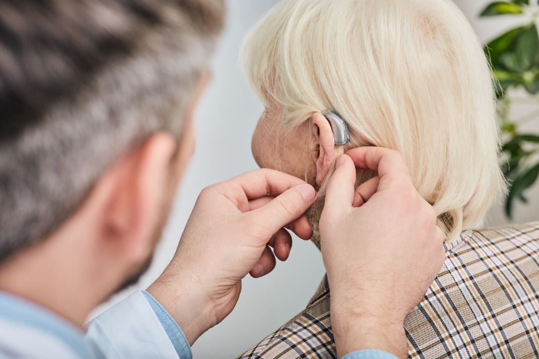 Audiologist adjusting hearing aid on elderly woman