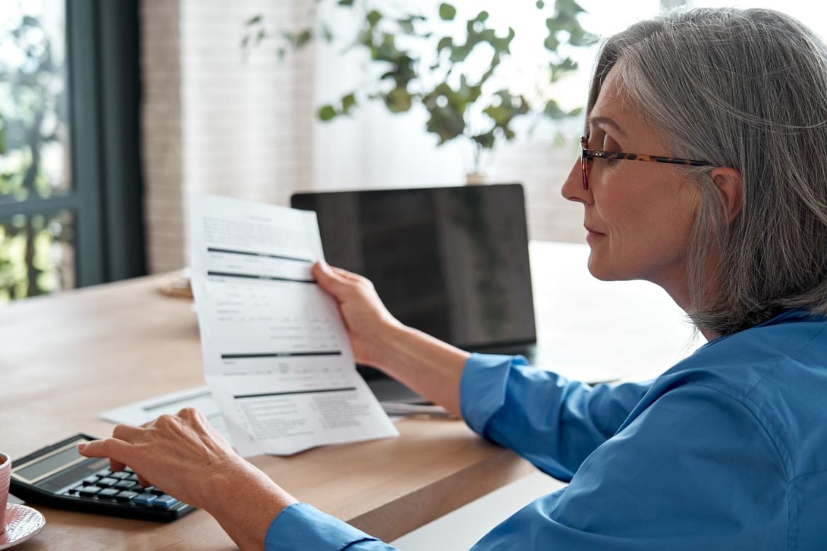 Woman reviewing paperwork and using calculator at desk