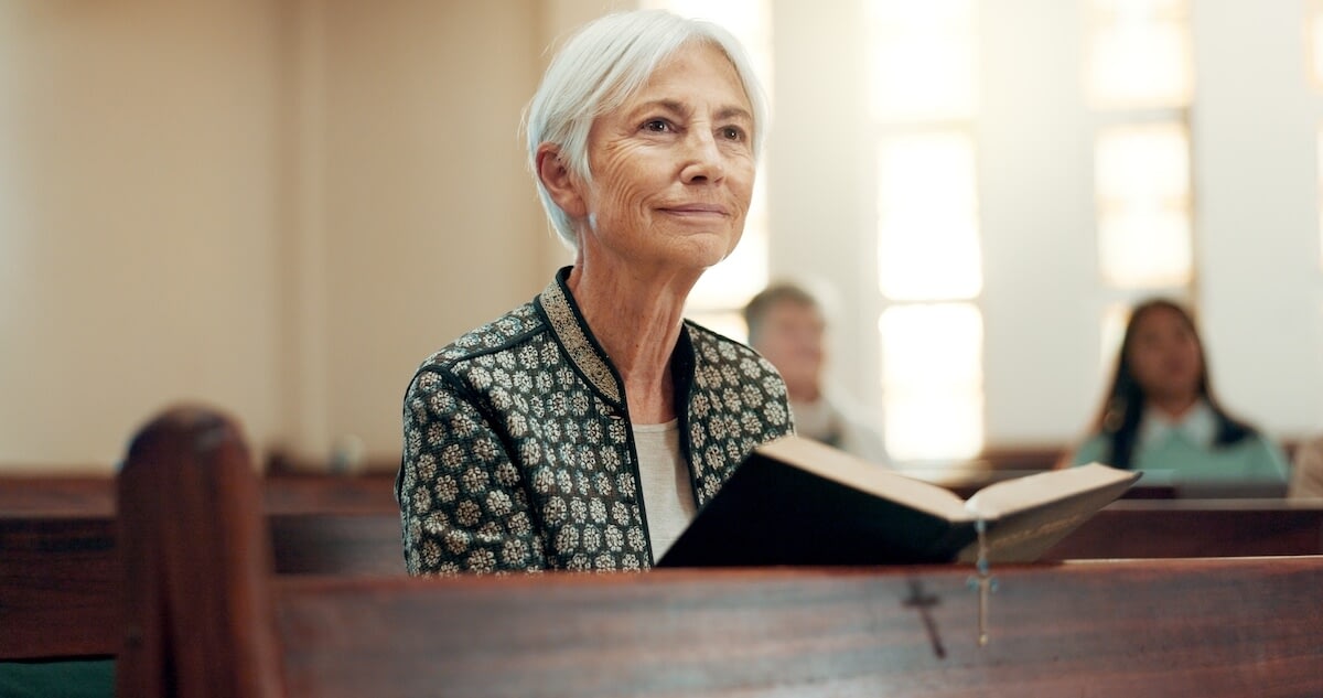 Elderly woman reading book in church pew