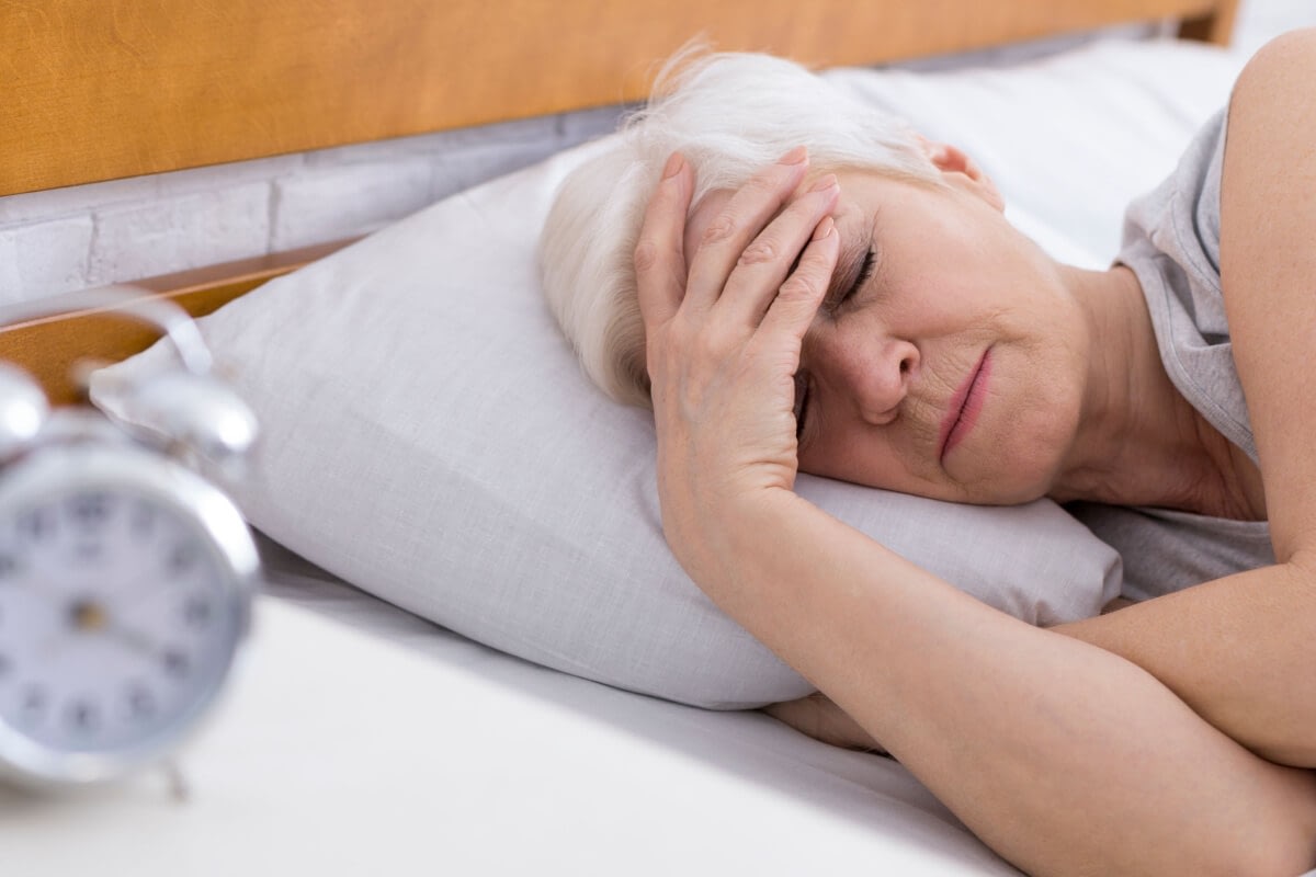 Elderly woman in bed holding her forehead