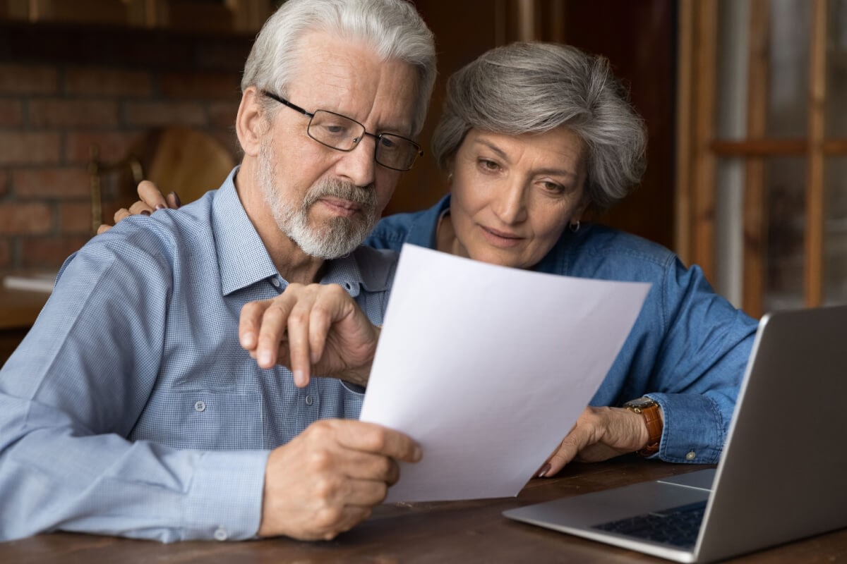 Senior couple reviewing document beside laptop