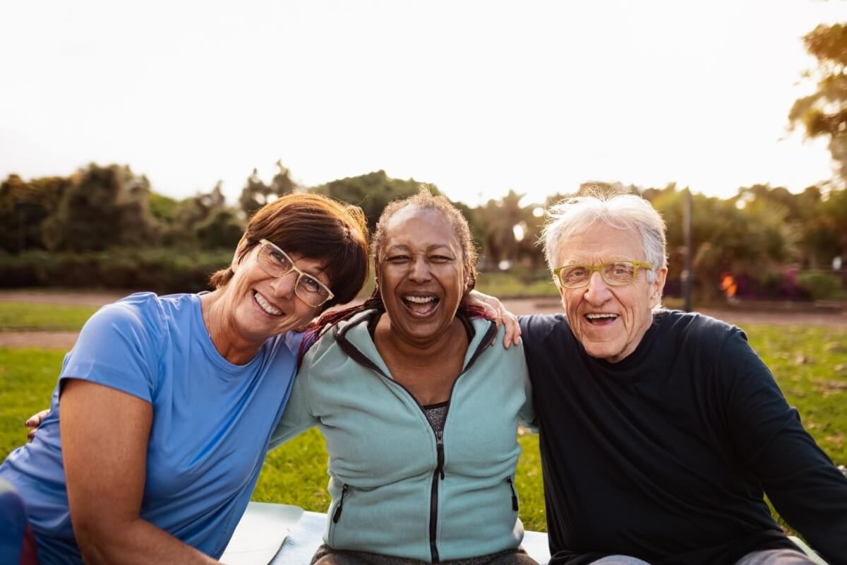 Three older friends smiling together in park
