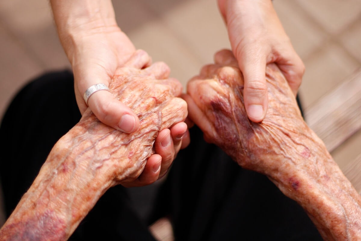 Caregiver holding elderly person's bruised hands