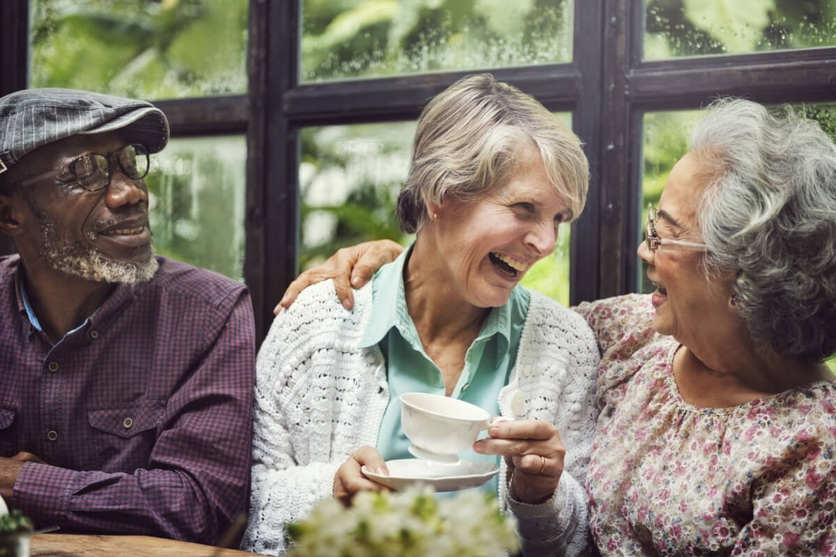 Three seniors laughing together over tea indoors
