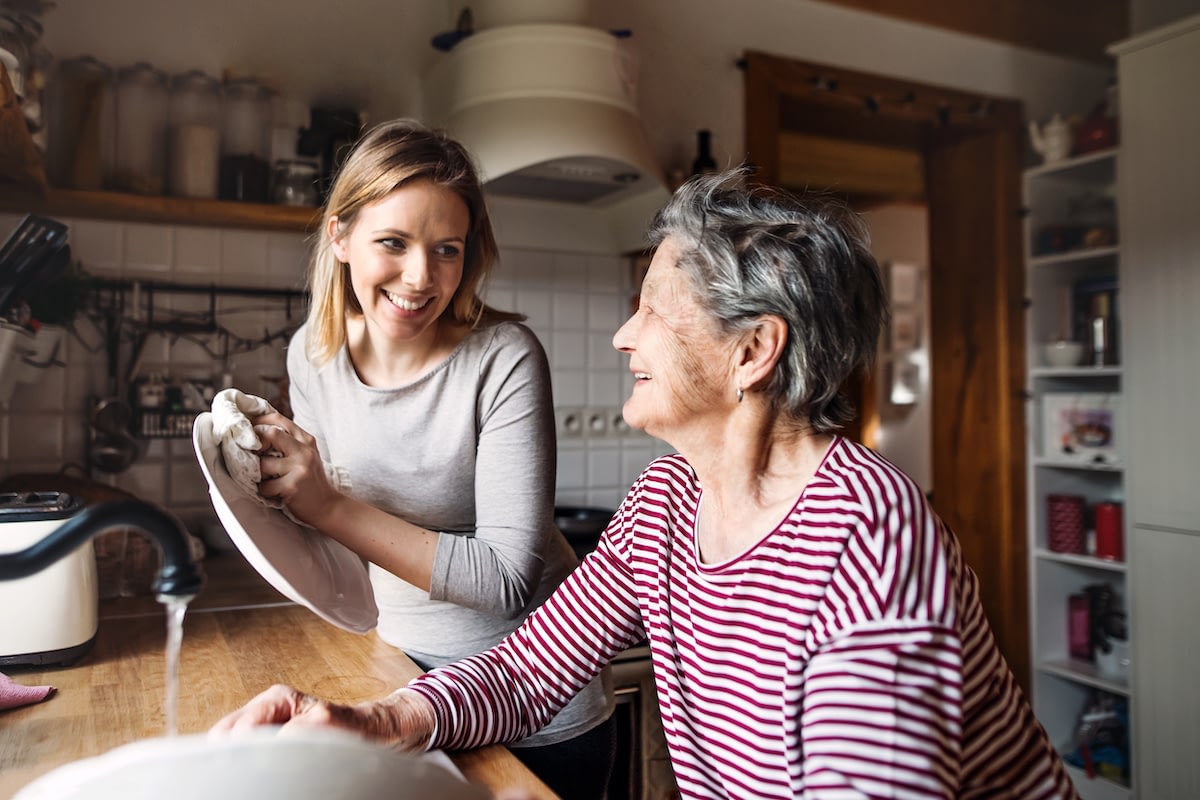 Young woman washing dishes with elderly woman