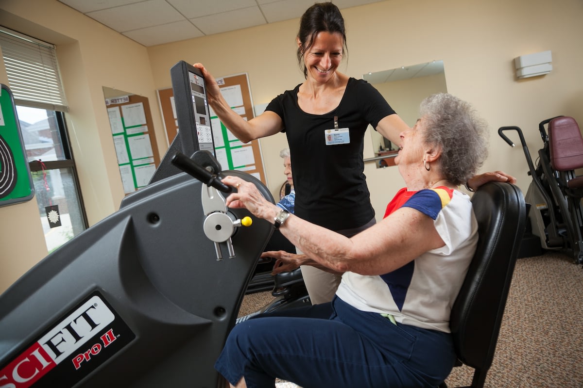 Senior woman exercising on machine with trainer
