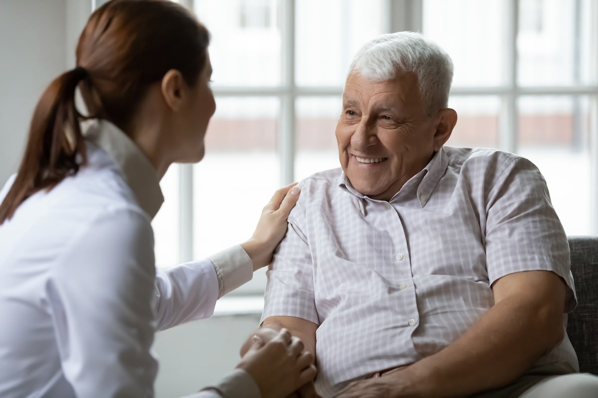 Healthcare worker comforting smiling elderly man indoors