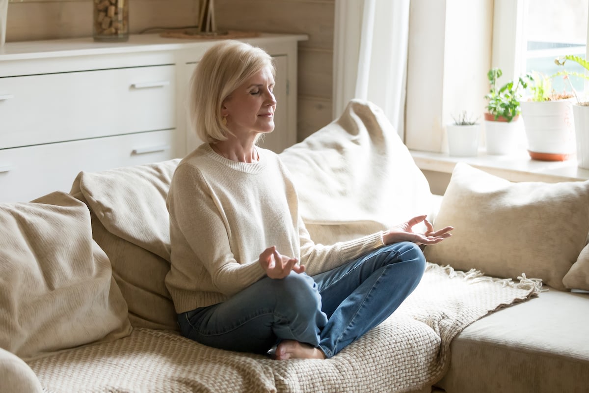 Woman meditating on couch in bright living room
