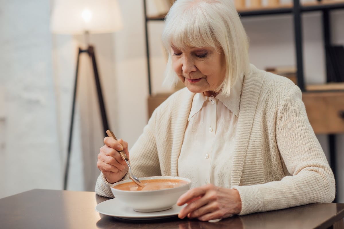 Elderly woman eating soup at dining table