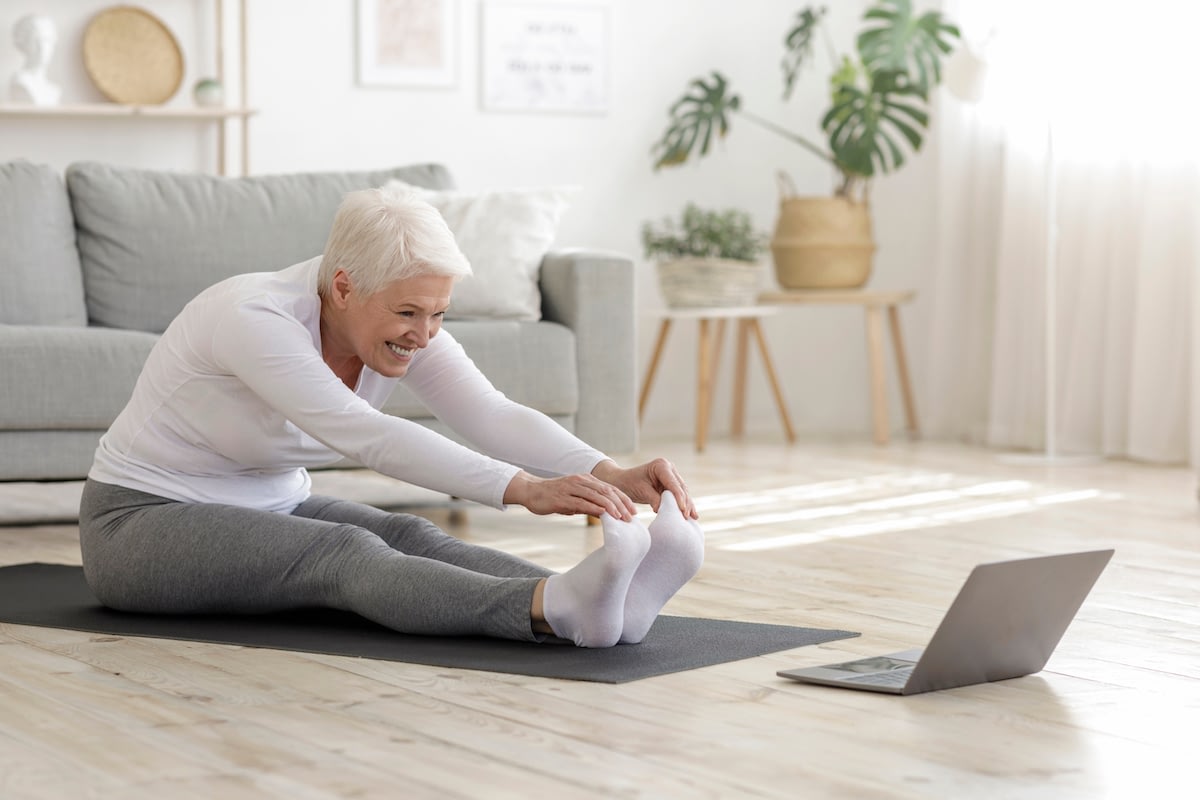 Senior woman stretching on yoga mat at home