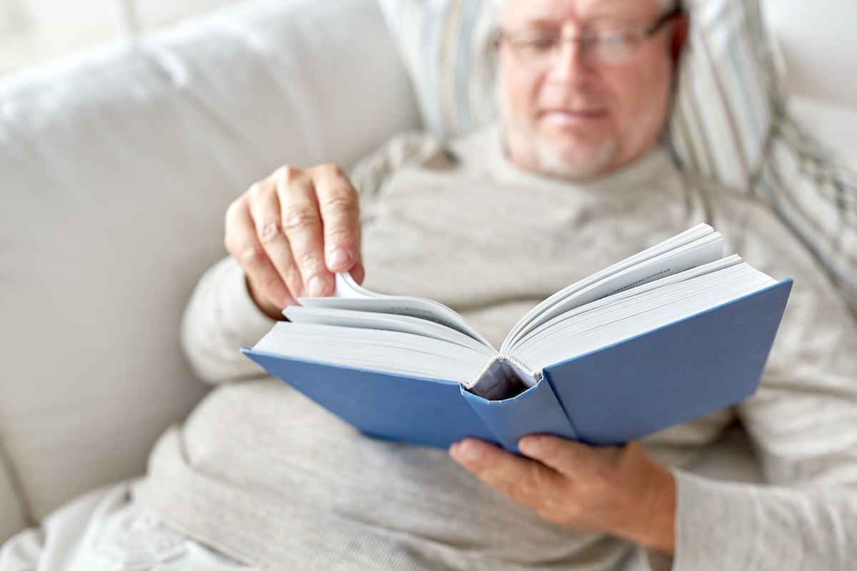 Older man reading blue hardcover book on couch