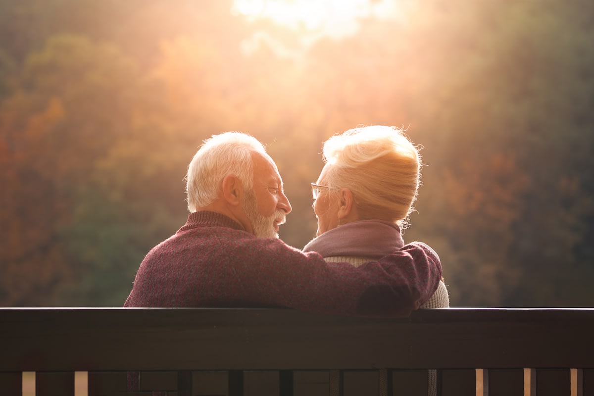 Elderly couple embracing on bench at sunset