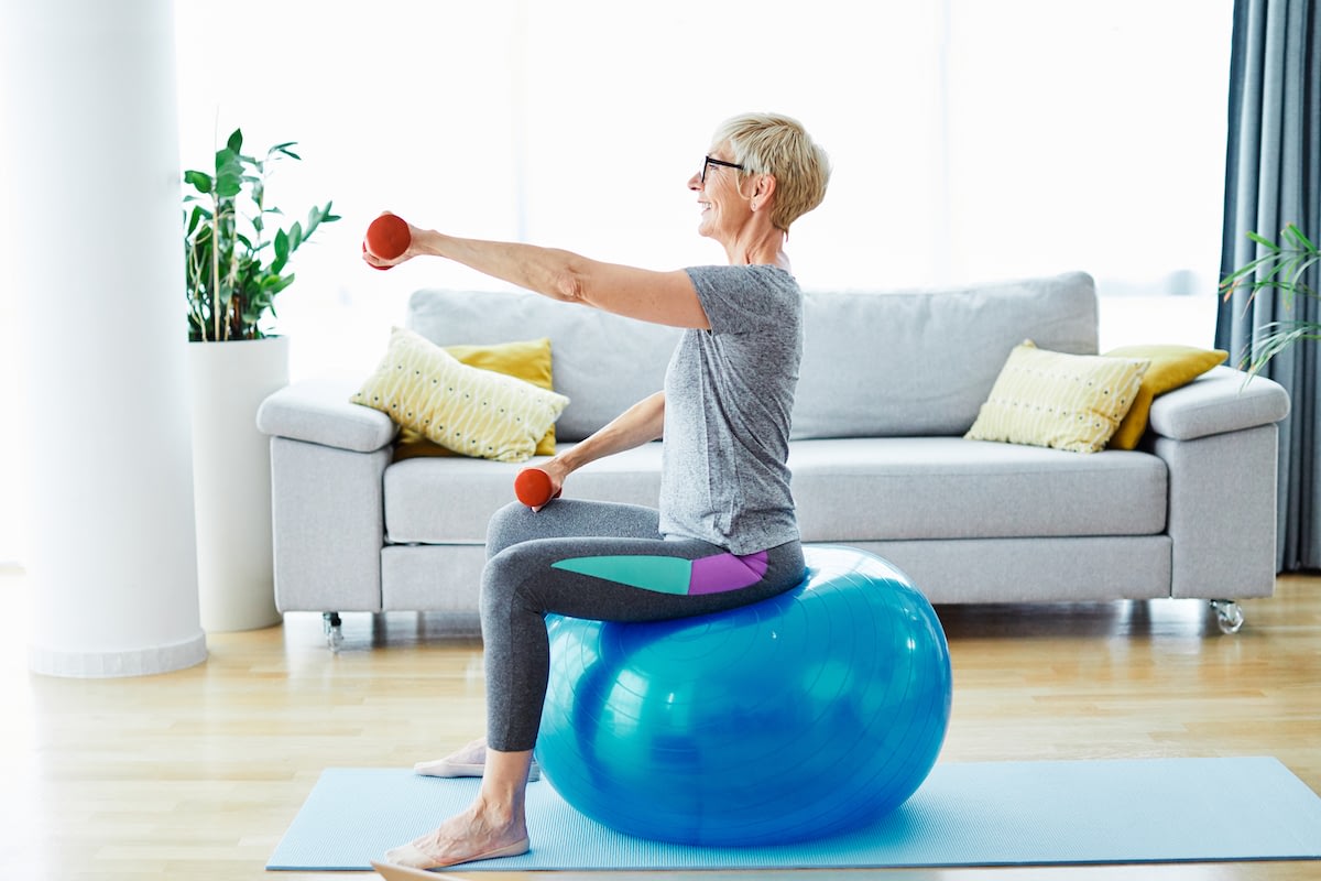 Senior woman exercising with dumbbells on stability ball