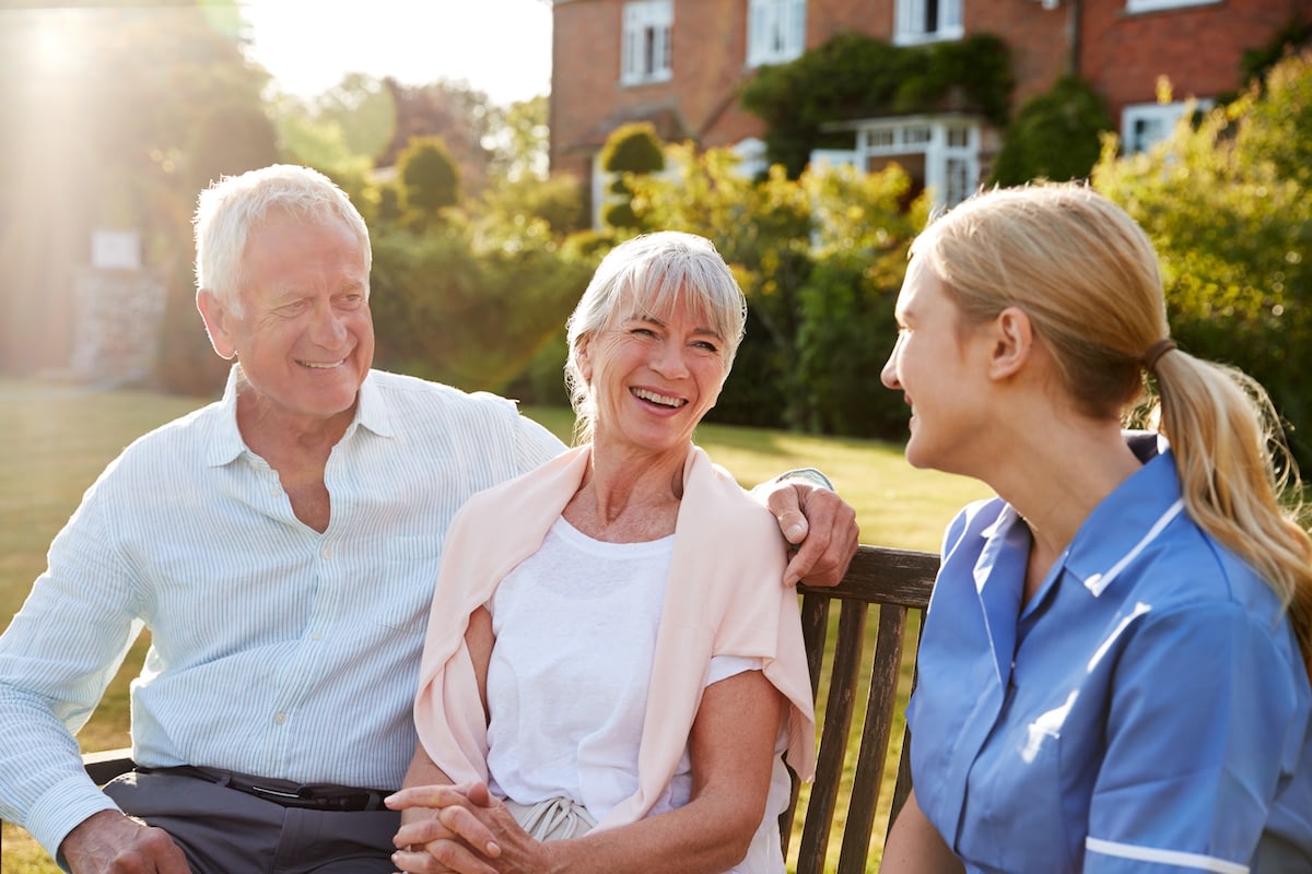 Elderly couple talking with caregiver on garden bench
