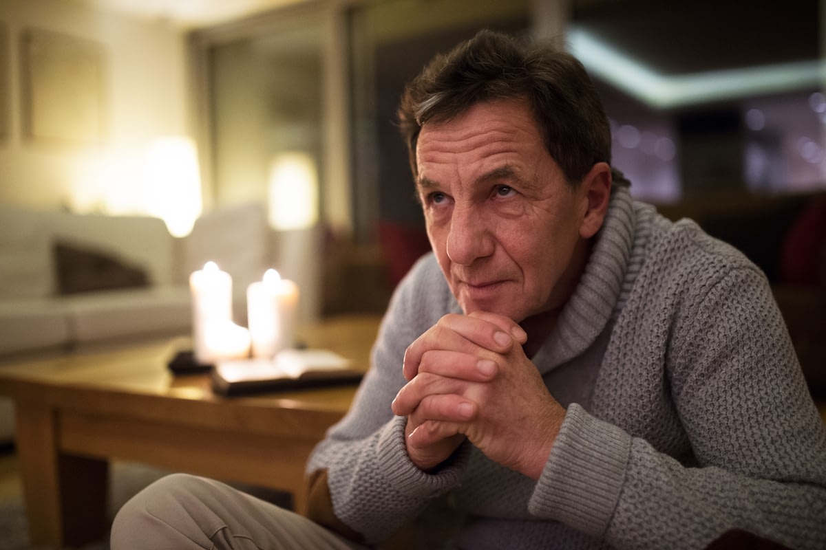 Middle-aged man reflecting by candlelight indoors