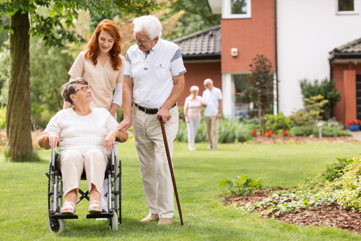 Elderly woman in wheelchair with caregivers outdoors