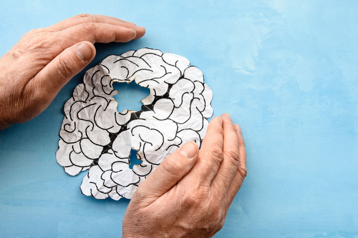 Elderly hands holding paper brain with holes