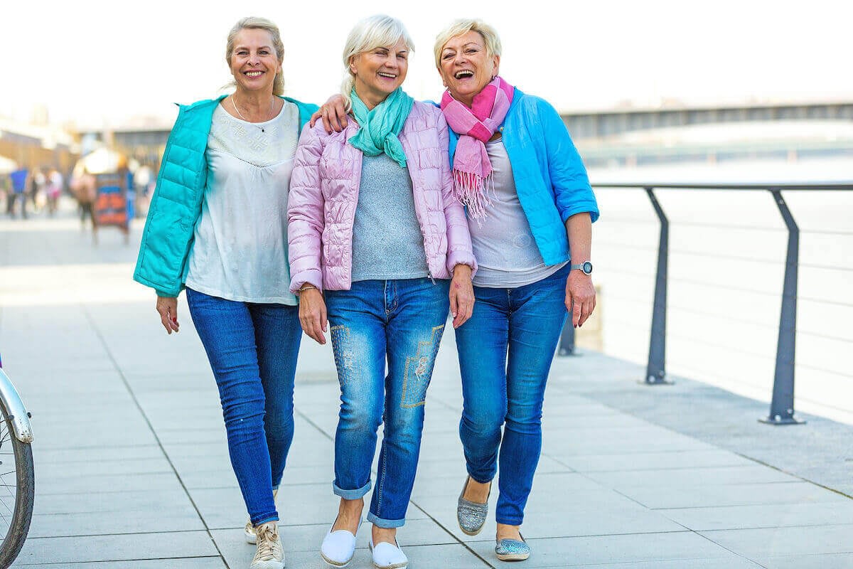 Three older women walking arm in arm outdoors