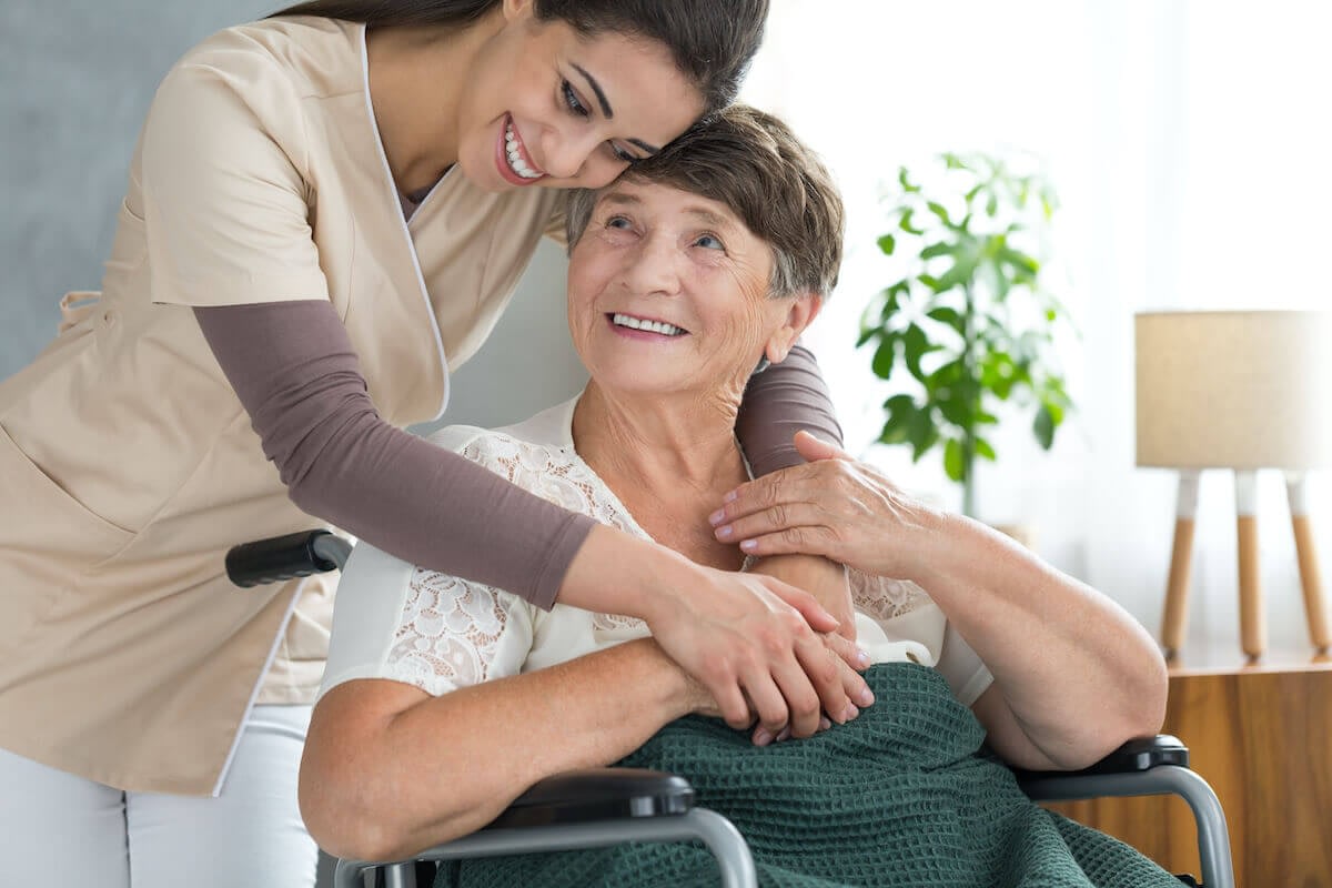 Caregiver hugging smiling elderly woman in wheelchair