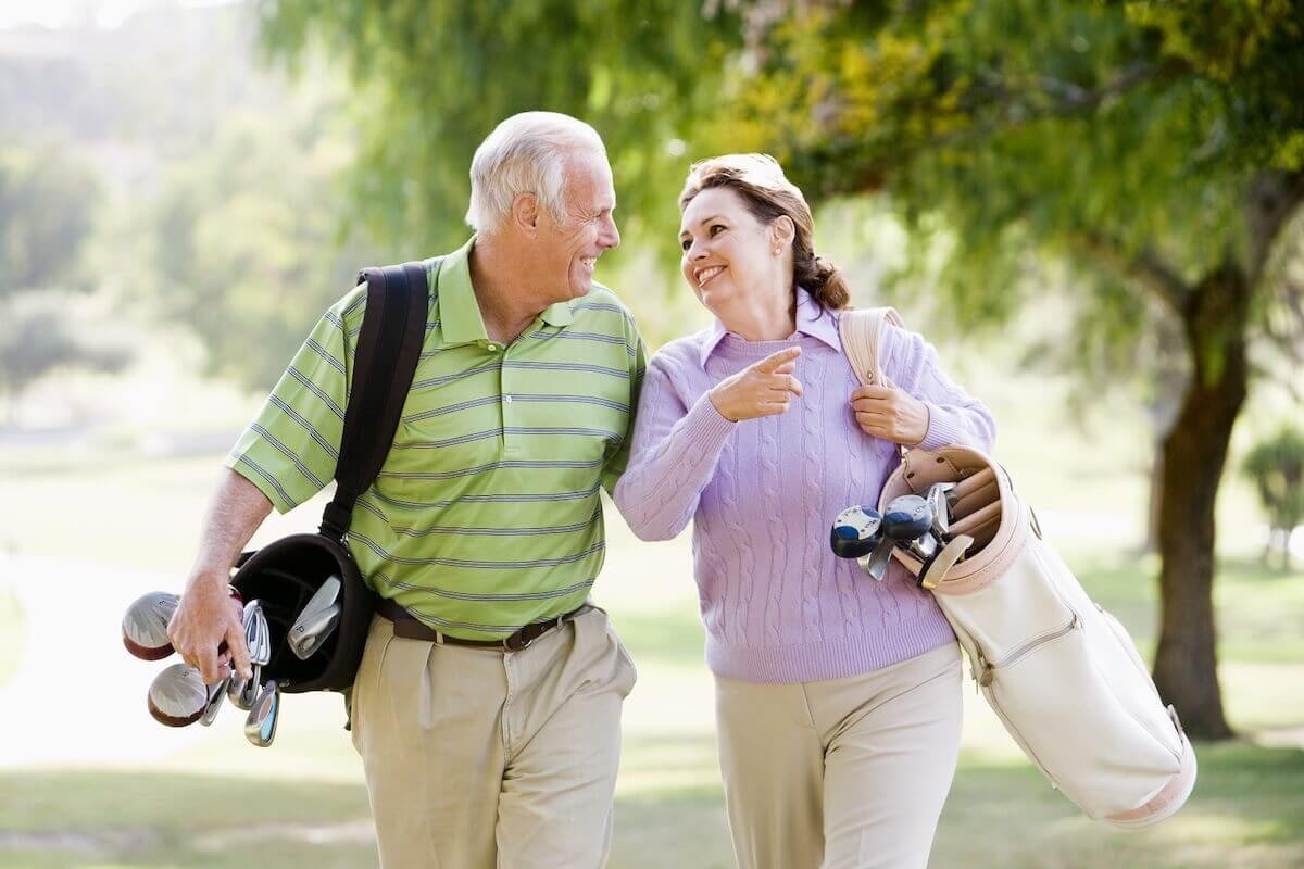 Senior couple walking with golf clubs outdoors