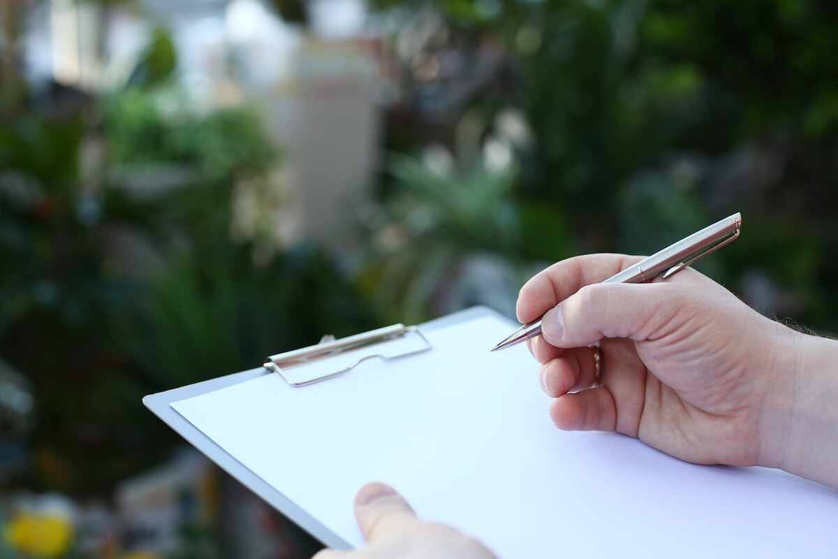Hand holding pen over blank clipboard outdoors