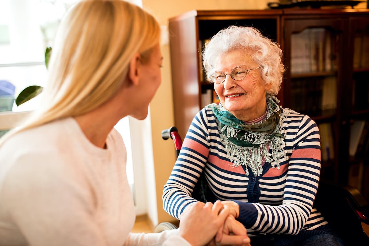 Caregiver holding elderly woman's hands at home