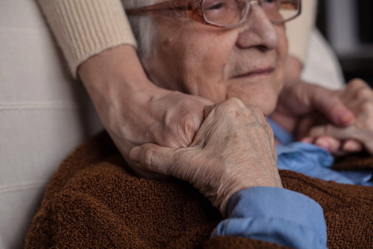 Elderly person holding caregiver’s hands closely