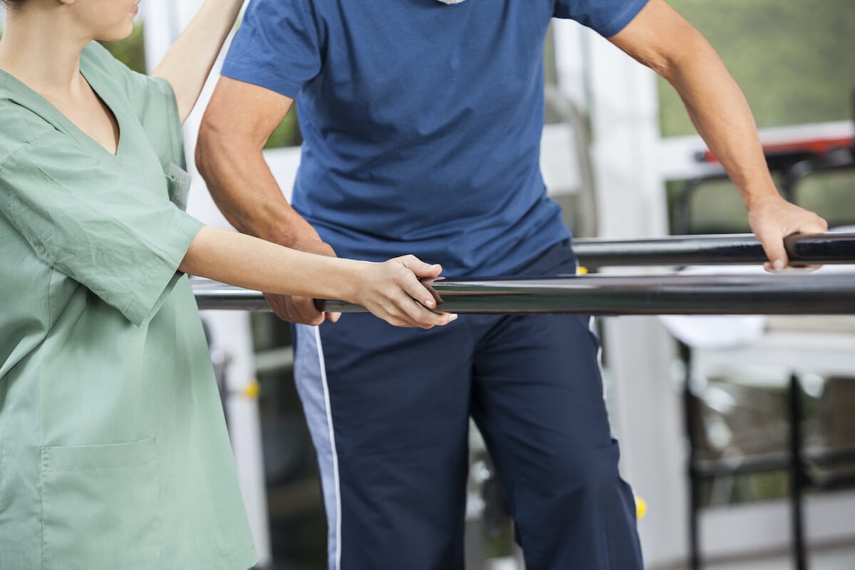 Therapist assisting patient with parallel bar rehabilitation