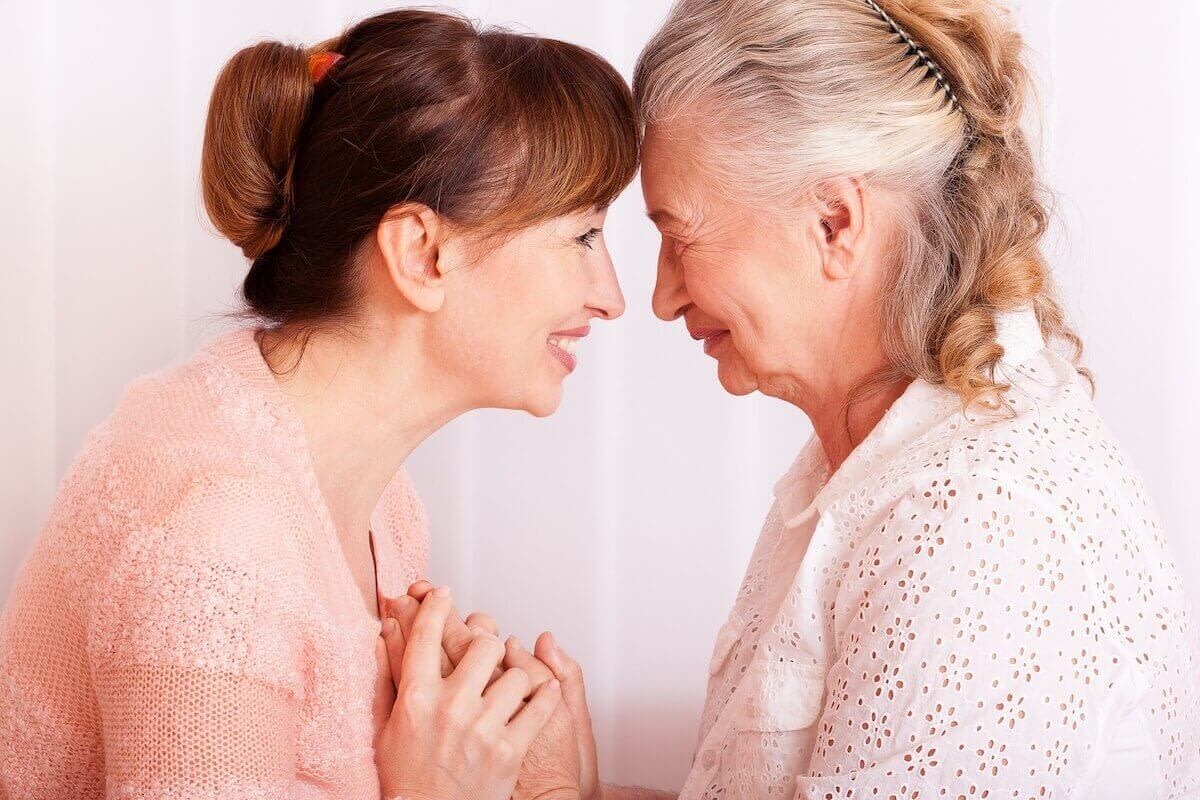 Adult daughter and elderly mother touching foreheads