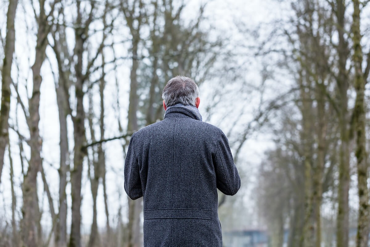 Man in gray coat walking forest path