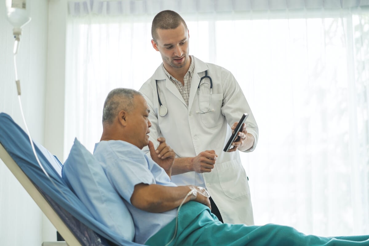 Doctor showing tablet to hospital patient in bed