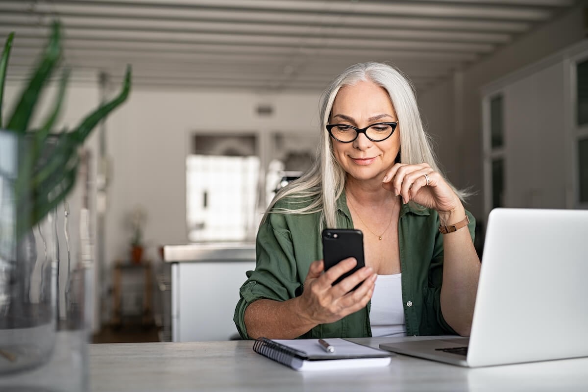Older woman using smartphone at home office desk