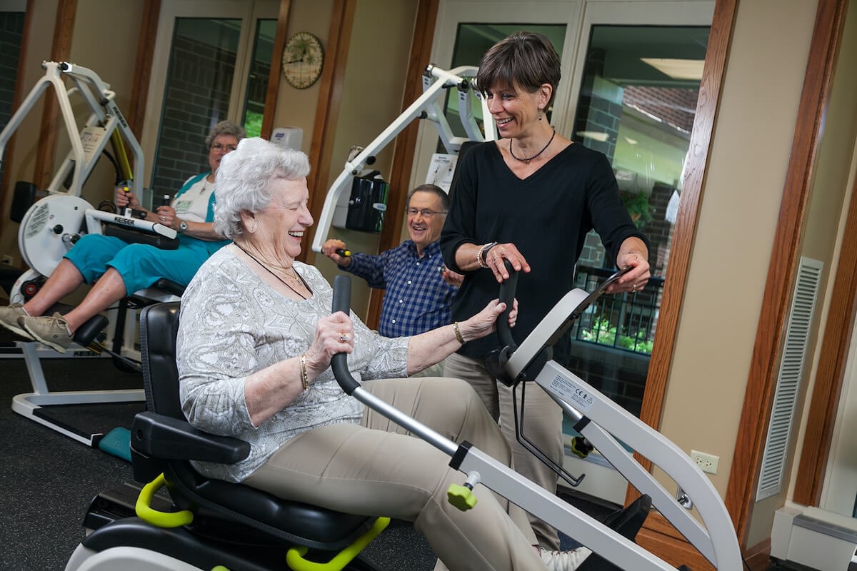 Senior woman exercising on machine with trainer
