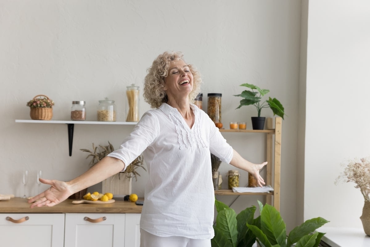 Smiling woman with arms outstretched in bright kitchen
