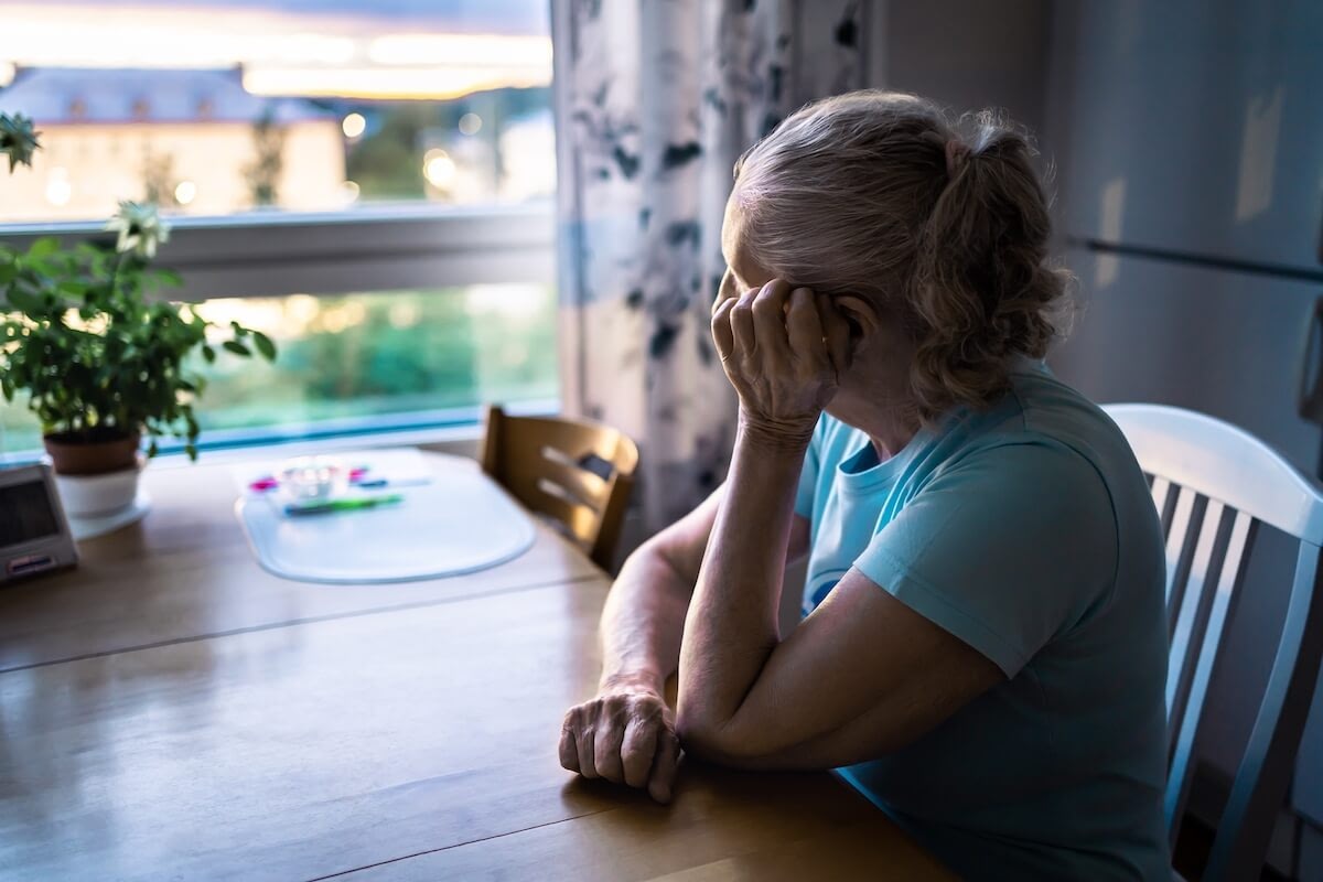 Elderly woman sitting at table looking out window