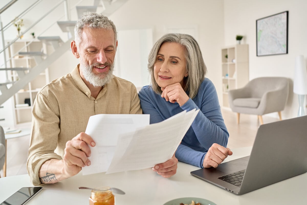 Older couple reviewing documents at home with laptop