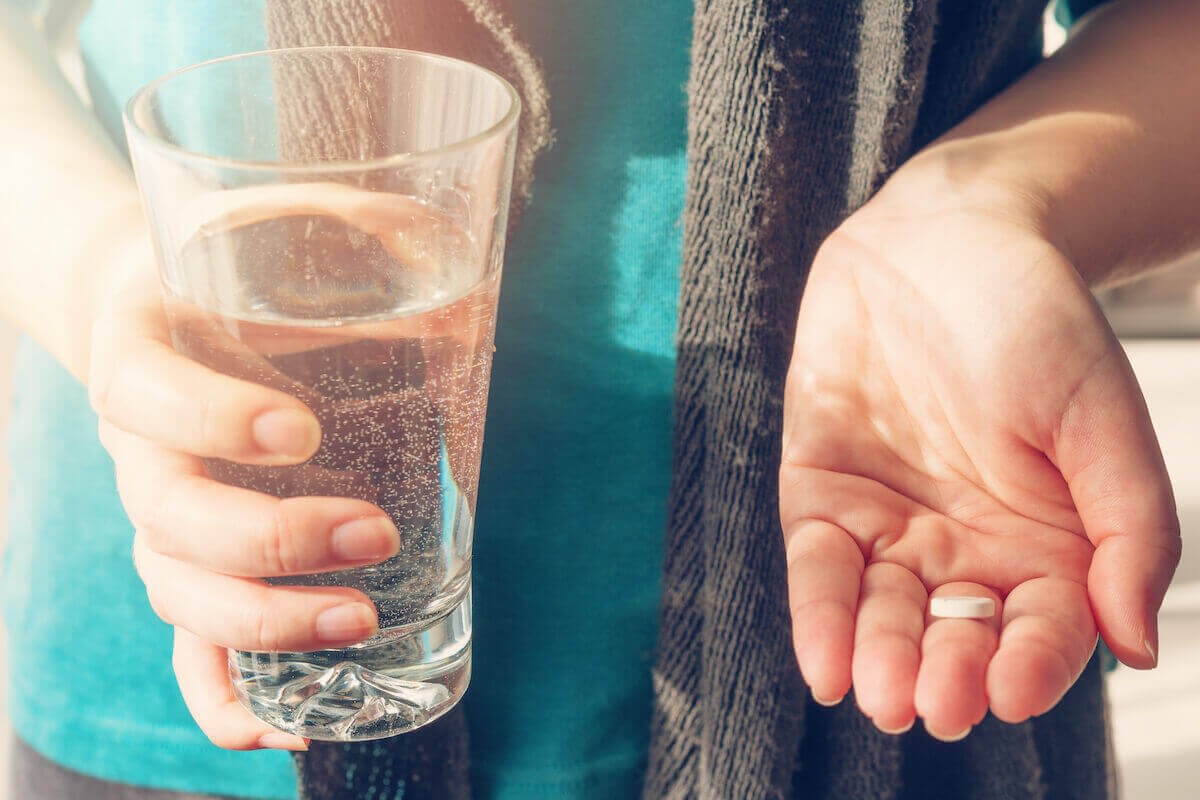 Person holding water glass and pill in hand