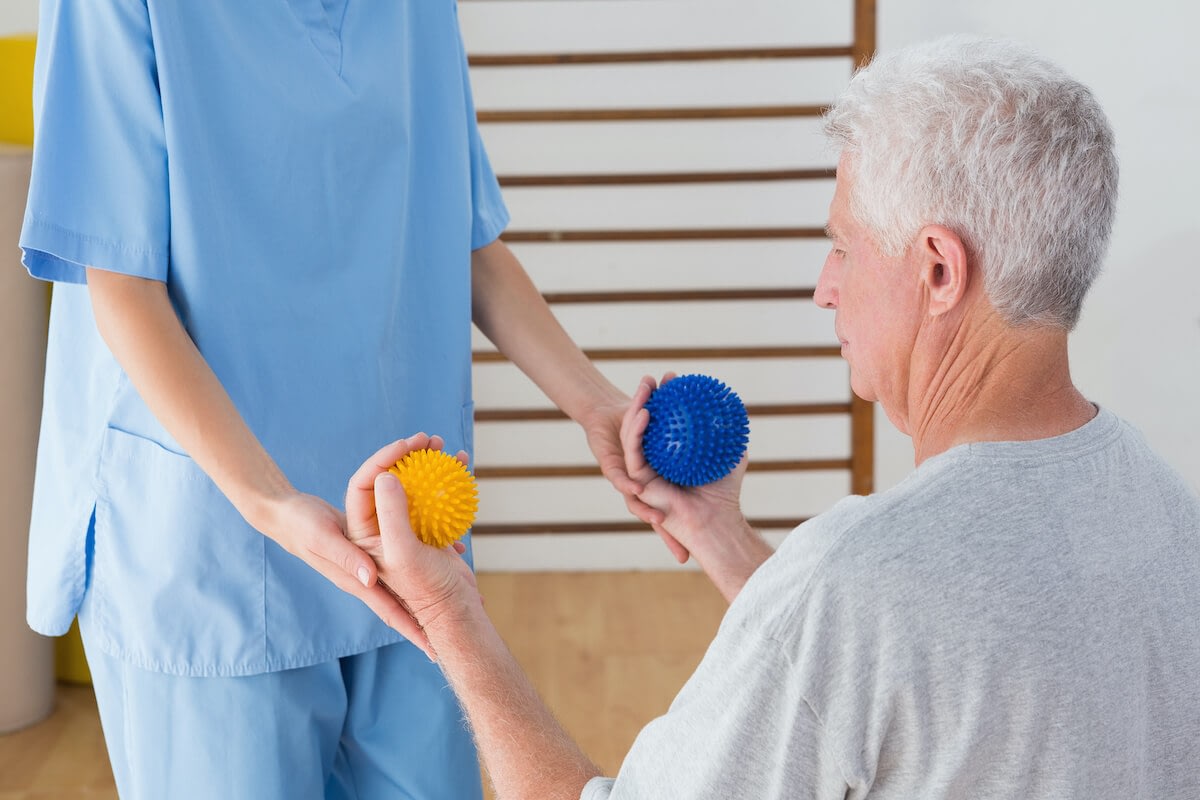 Senior man squeezing therapy balls with caregiver.