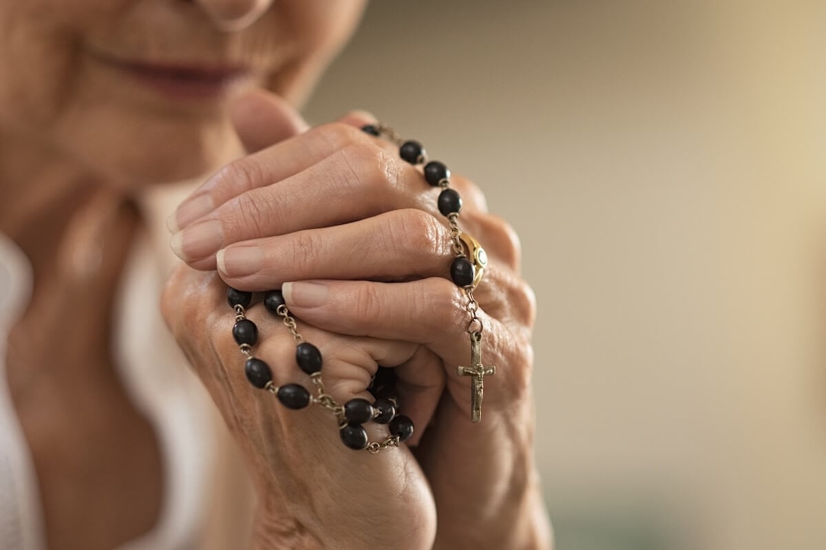 Elderly woman holding rosary and praying
