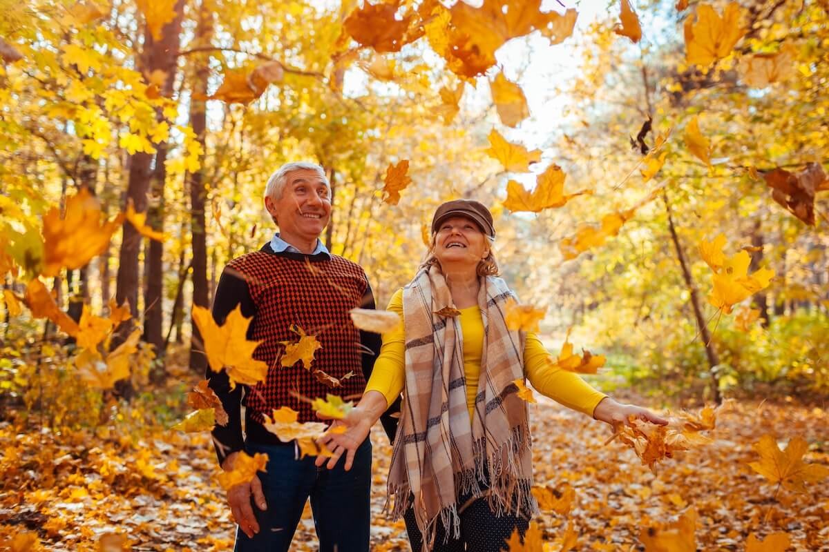 Senior couple enjoying falling autumn leaves outdoors