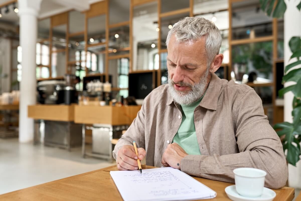 Gray-haired man writing at cafe table
