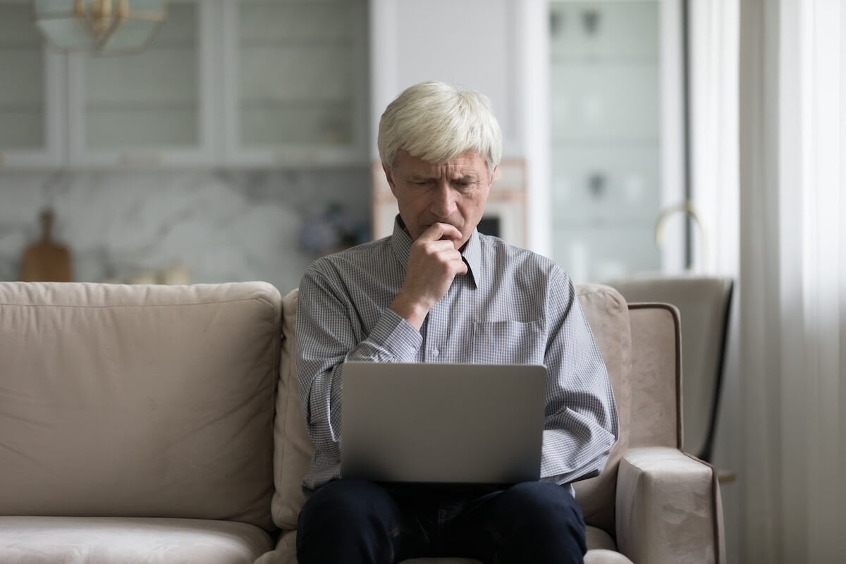 Older man looking concerned at laptop on couch