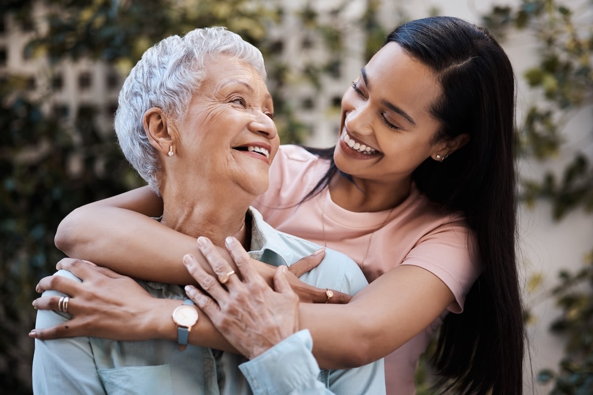 Young woman hugging smiling elderly woman outdoors